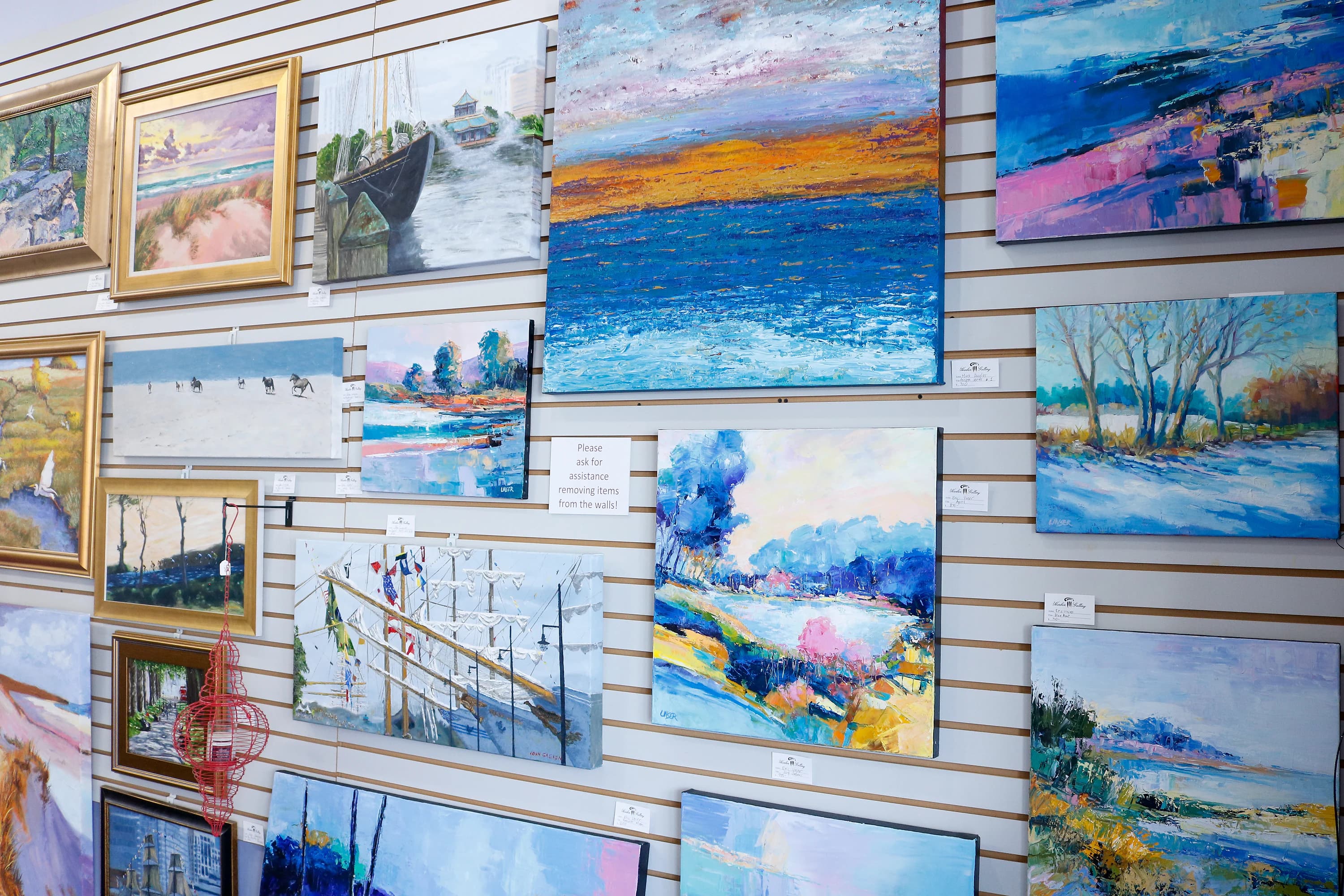Seascape and landscape paintings filling a gallery wall